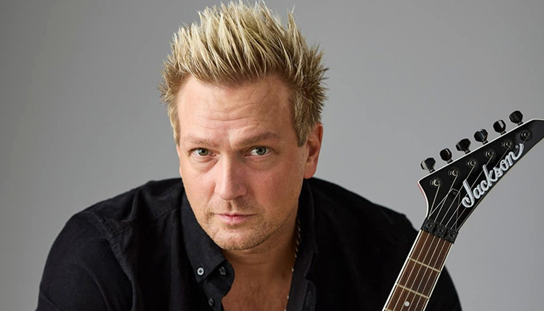 Svartklädd blond man, gitarr sticker fram.