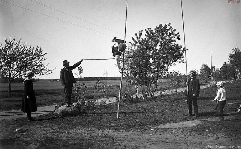 Svartvitt gammalt foto av man som hoppar stavhopp.