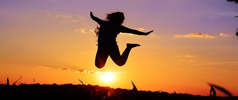 En kvinna hoppar. I bakgrunden syns en solnedgång.